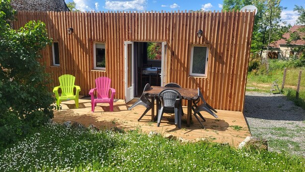 A wooden cabin with two doors, a table with chairs, and two Adirondack chairs. - Mobil chalet (Blars)