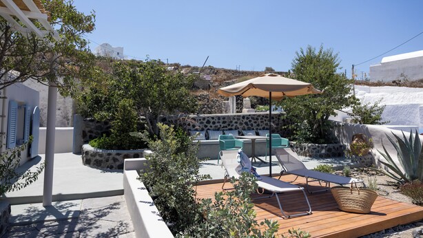 A sunlit outdoor patio with lounge chairs, a table, and a large umbrella.