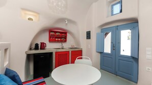 A compact kitchen with a sink, a dishwasher, and a red dish rack. There is a white table and a blue door in the background.