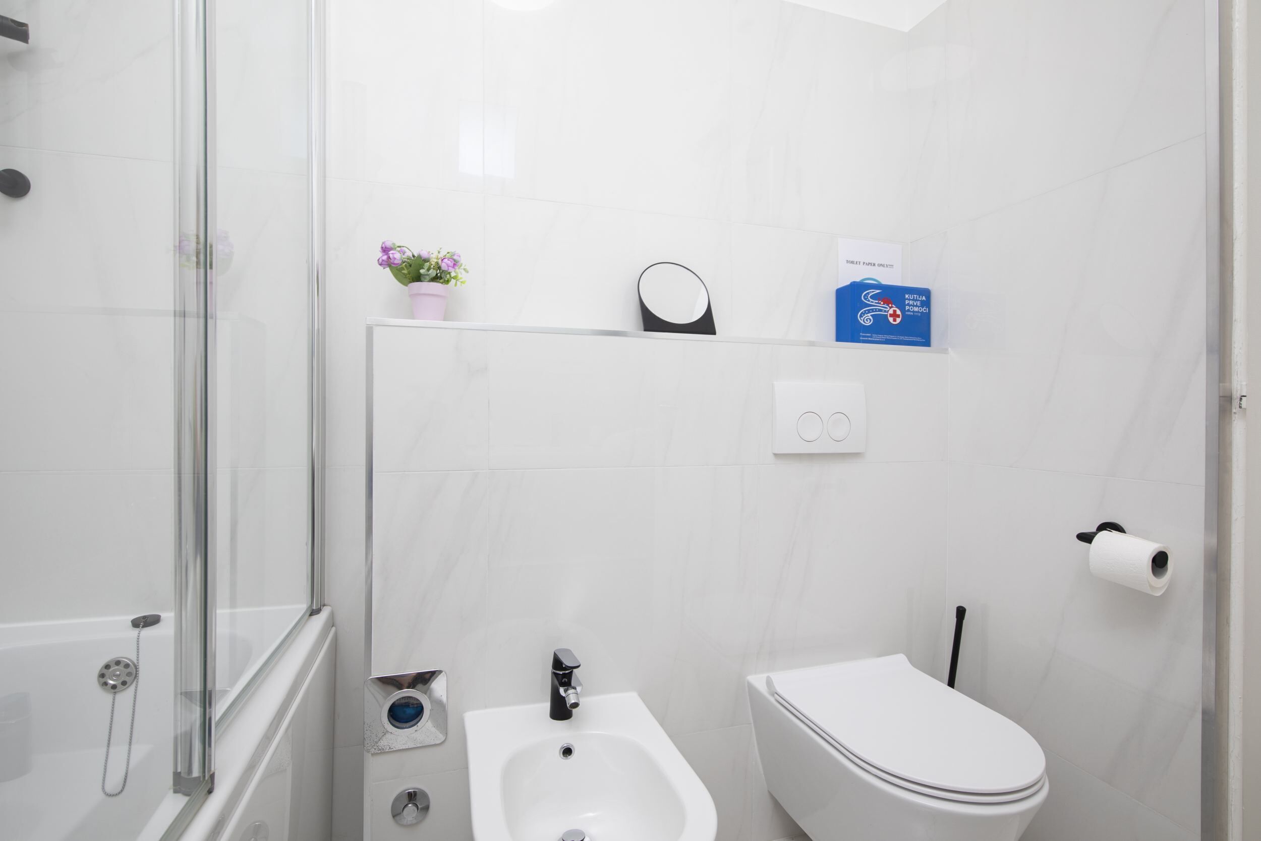 Ein modernes Badezimmer mit Duschkabine aus Glas, einem Bidet, einer Toilette und einer kleinen Ablagefläche für Toilettenartikel.