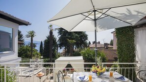 An outdoor dining area with a table set for two, a white umbrella, and a view of the sea.