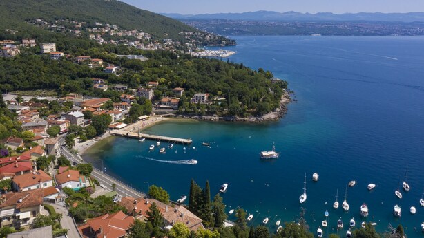 A coastal town with a marina, buildings, and a hilly backdrop.