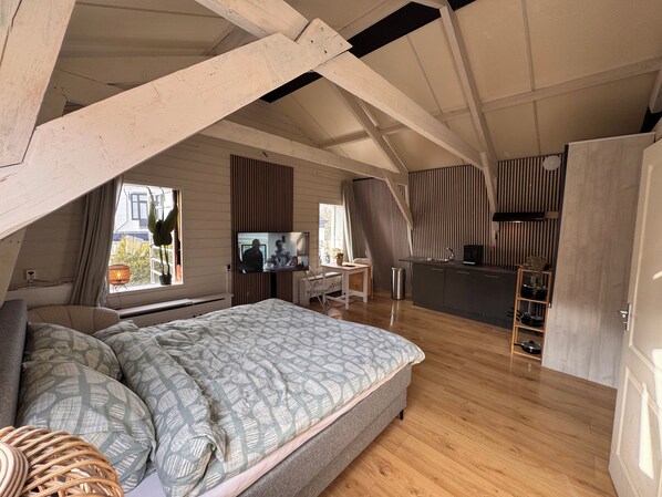 A compact, loft-style bedroom with a bed, a desk, and a kitchenette.