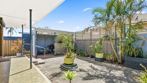 Un patio couvert comprenant un barbecue, des sièges d’extérieur et diverses plantes en pot.