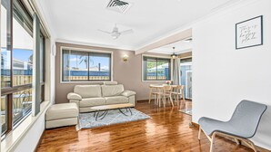 Un vaste espace de vie agrémenté d’un canapé beige, de parquet et de grandes fenêtres offrant une vue sur la mer.