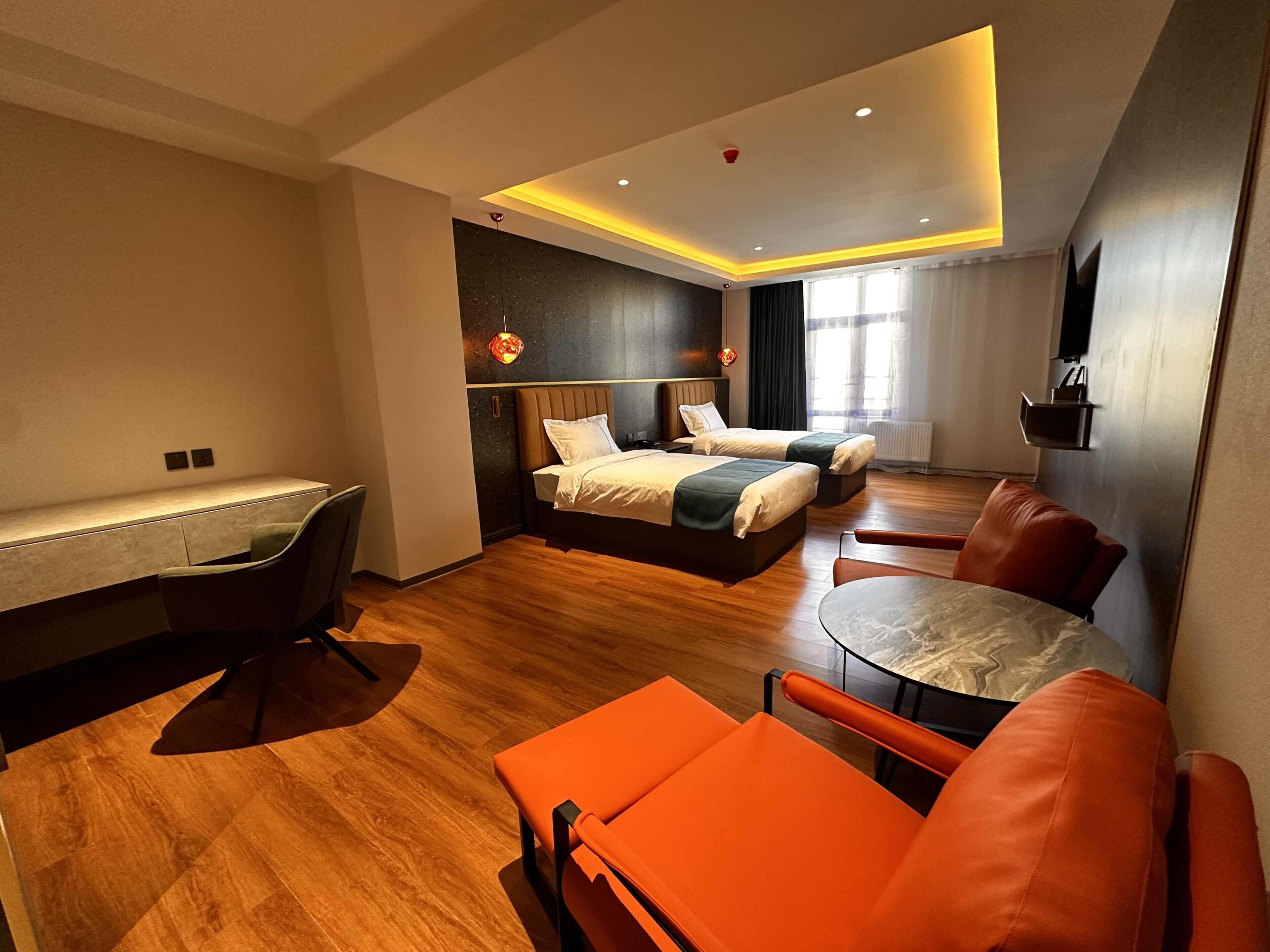 Quarto de hotel moderno com escrivaninha, duas camas, uma mesa de jantar e cadeiras laranja.