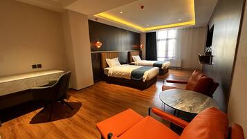 Quarto de hotel moderno com escrivaninha, duas camas, uma mesa de jantar e cadeiras laranja.