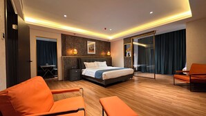Una habitación de hotel moderna con una cama grande, un escritorio, un sofá naranja y un banco.