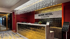 Zona de recepción de un hotel con diseño moderno, que incluye un mostrador de recepción, un cartel que dice "BOJON HOTEL ULAANBAATAR" y una pared con motivos decorativos detrás del mostrador.