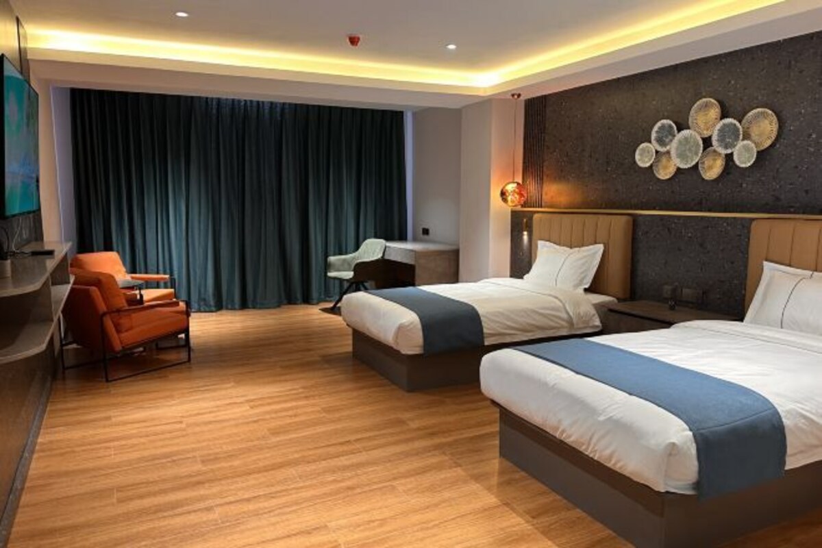 A hotel room with two beds, a desk, a chair, and a large window with curtains.
