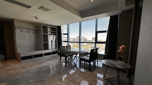 Una habitación de hotel moderna con un ventanal grande, una zona de estar con mesa y sillas, y un armario empotrado con batas colgadas.