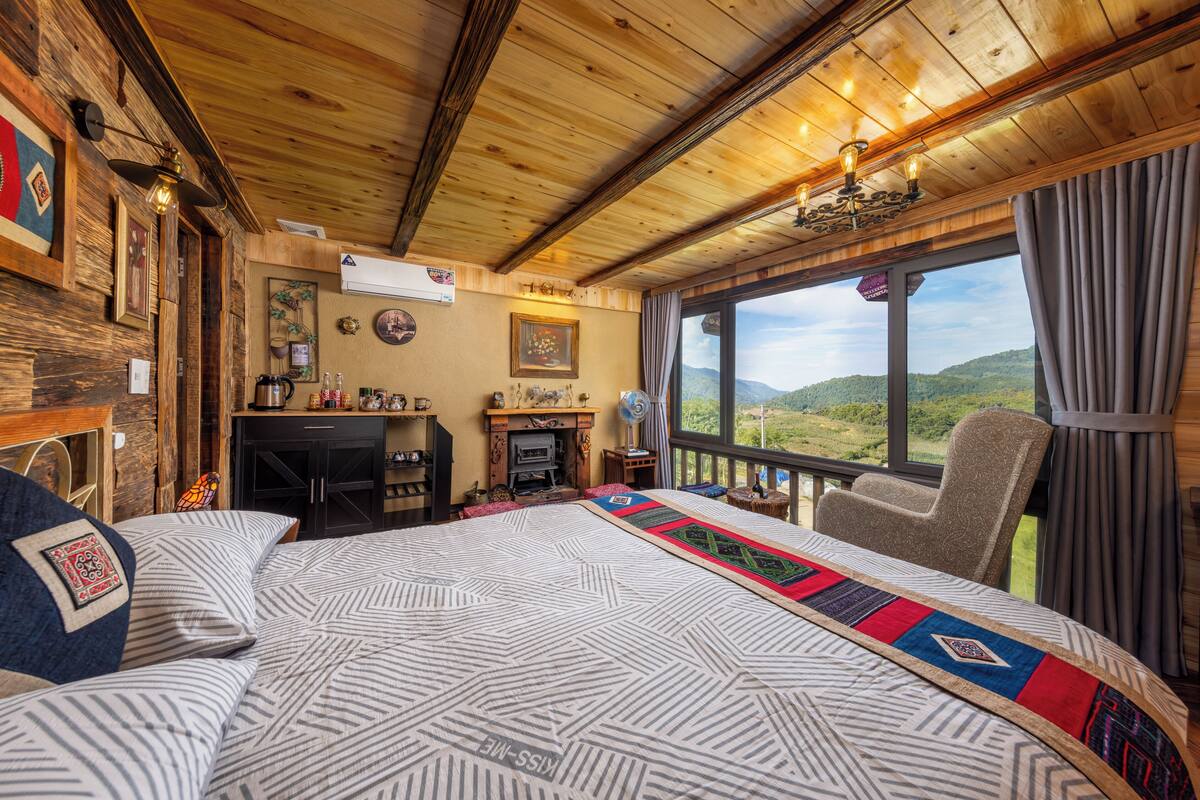 A wooden interior with a bed, a fireplace, and a view of the outdoors.