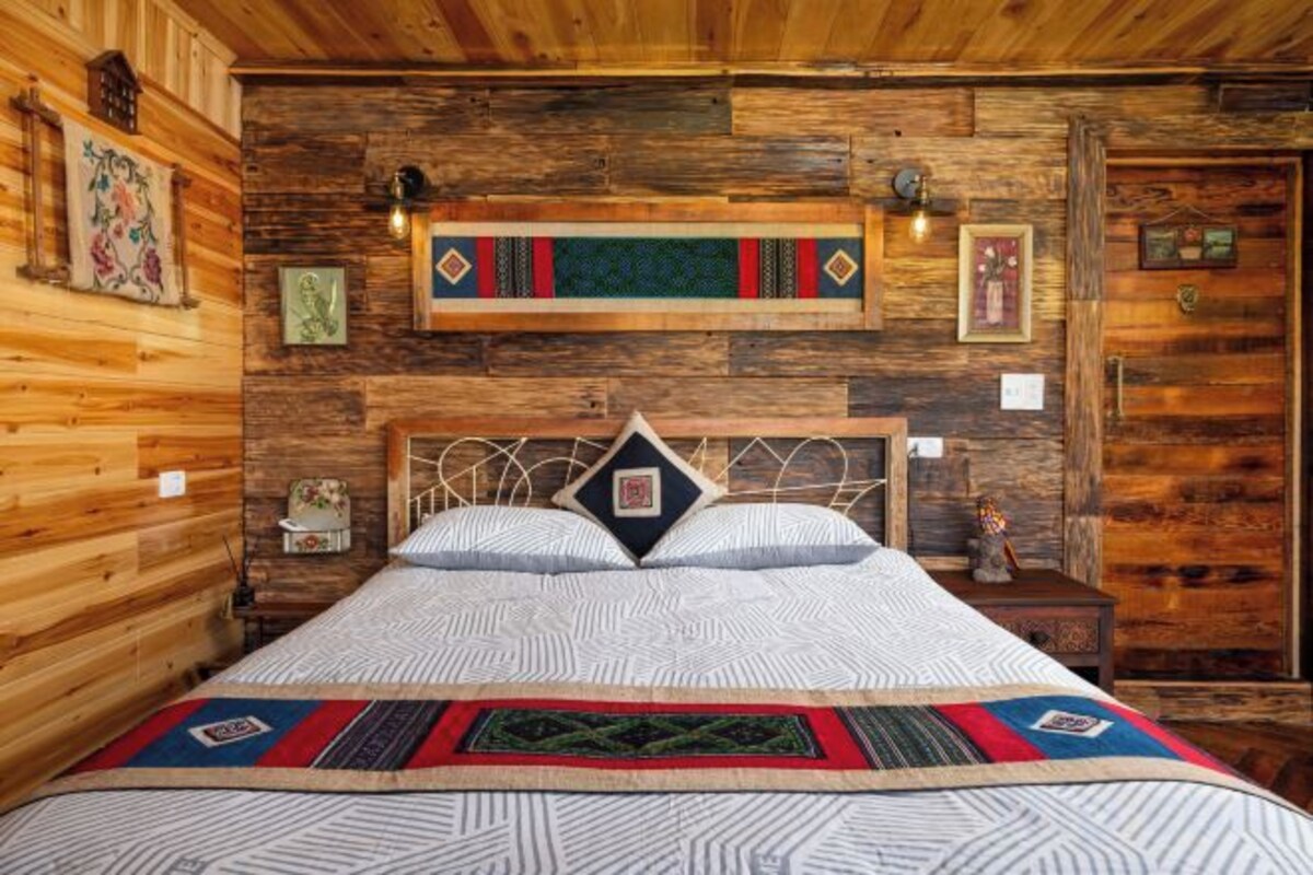 Una habitación con paneles de madera, una cama, un estante en la pared y una puerta.