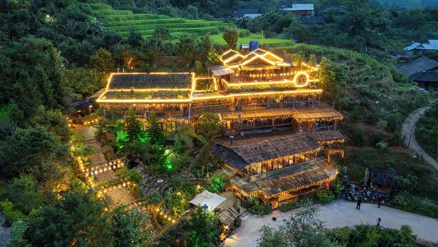 A multi-story building with a rustic design, surrounded by lush greenery and terraced fields.