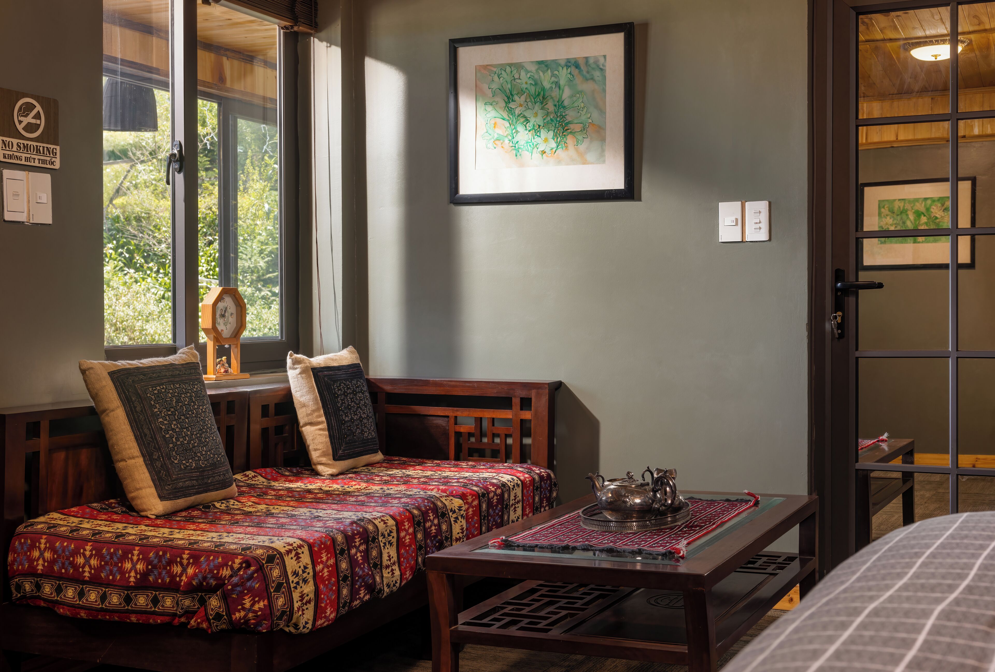 Una habitación tradicional con cama, una mesa con tetera y ventana con vistas a vegetación.