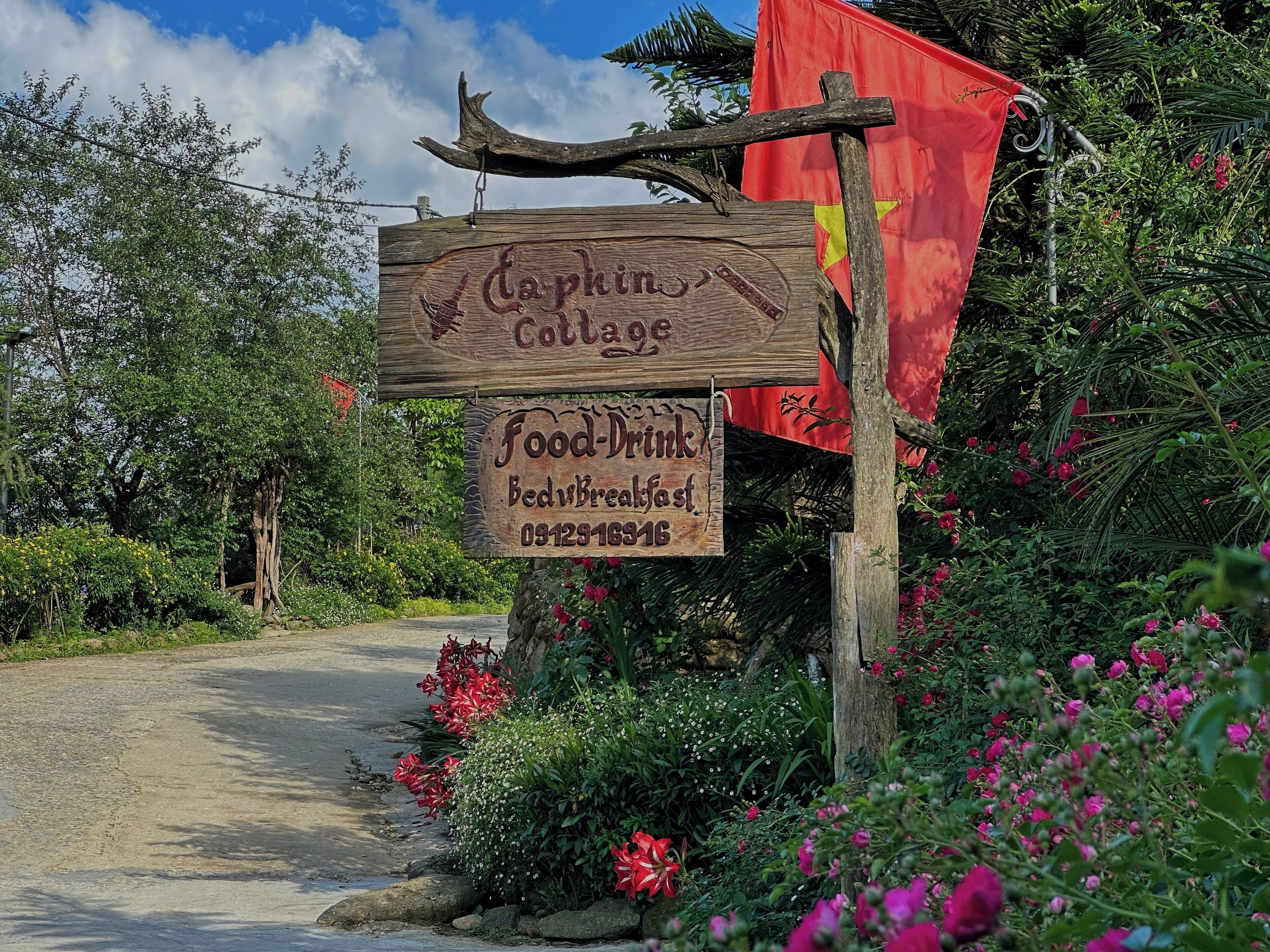 A wooden sign for 'Captain's Cottage' with a food and drink service, surrounded by lush greenery and a red flag.