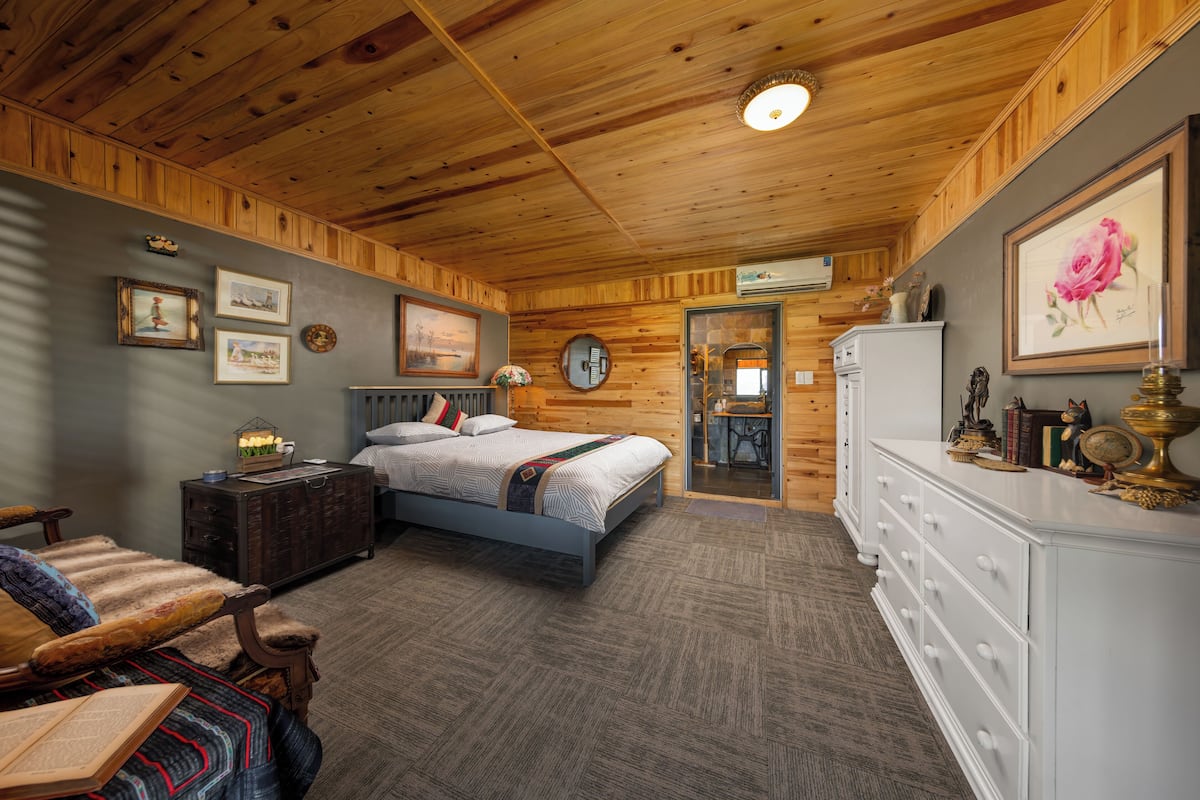 A cozy room with a wooden ceiling, a bed with a headboard, a dresser, and a chair.