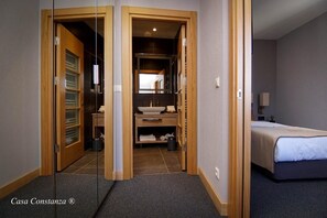 Ett hotellrum med en säng, ett badrum med handfat och spegel samt en garderob med hyllor.