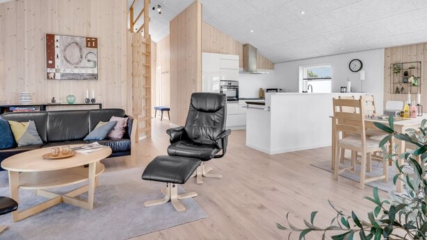 A modern living space with a wooden floor, a black leather sofa, a dining table, and a kitchen area with white cabinets. - "Ebertine" - 740m to the fjord by Interhome (Storvorde)