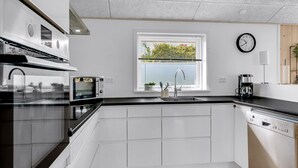 A modern kitchen with white cabinetry, a black countertop, a built-in oven, a microwave, a sink with a faucet, a window with a view of greenery, and a clock on the wall. - "Ebertine" - 740m to the fjord by Interhome (Storvorde)