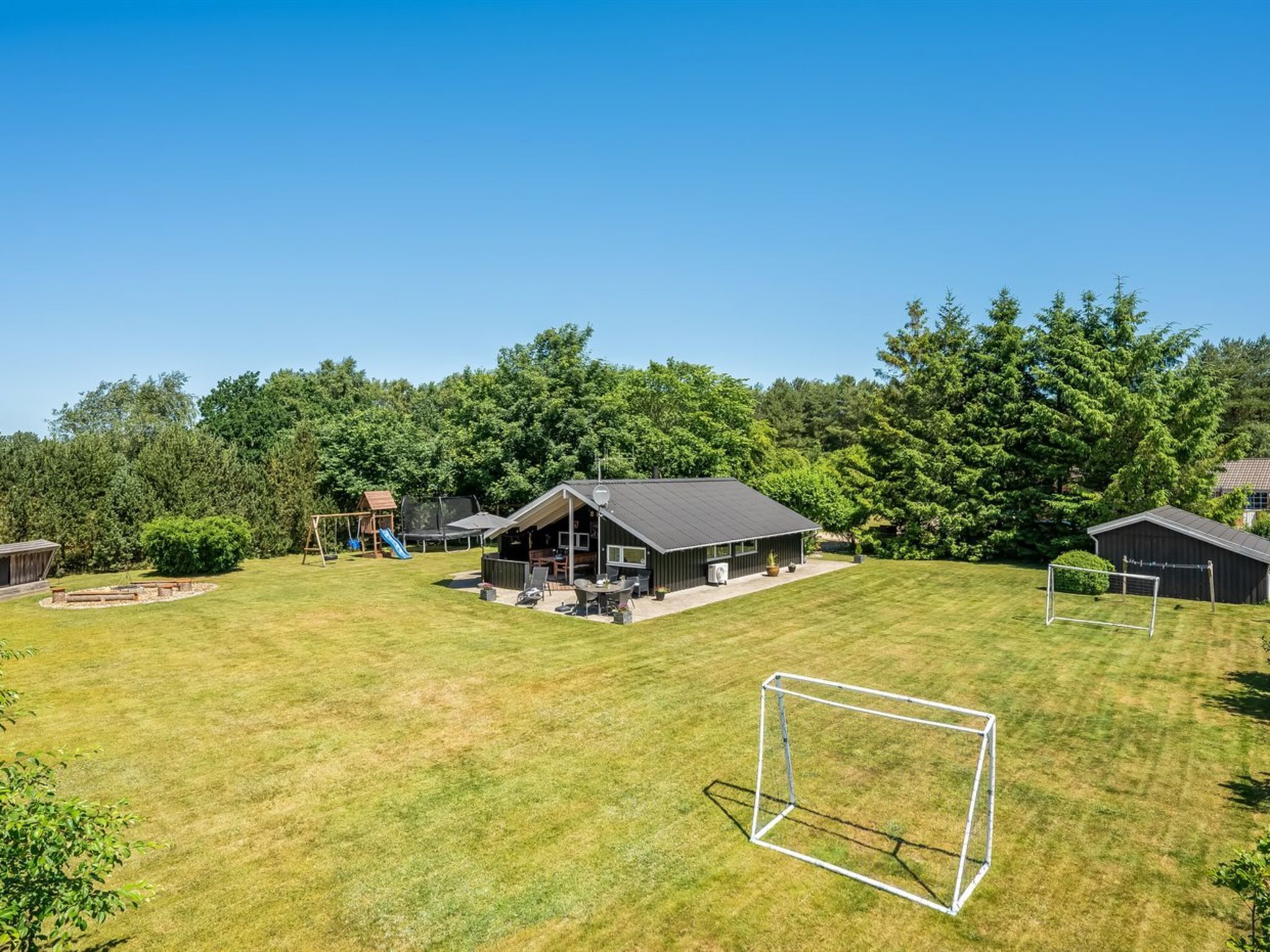 A residential property with a large lawn, a wooden play structure, a covered patio, and a small shed.