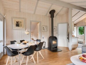 A modern interior with a central dining area, a black wood-burning stove, and a view of the outdoors.