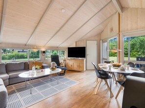 A spacious living area with a sofa, coffee table, and dining table, a flat-screen TV, and a kitchen area with wooden cabinets.
