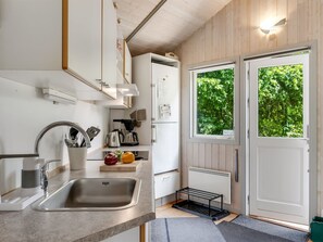 Cocina moderna con lavaplatos, estufa y refrigerador. Se ve una ventana con vista a árboles.