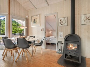 A cozy room with a fireplace, wooden walls, a dining area with chairs, and a bed in the background.