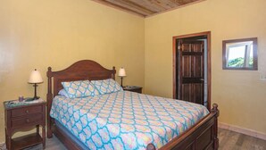 A bedroom with a wooden bed, two bedside tables, and a door. - 2-bedroom condo in West End at Sunset Villas with WiFi, AC and Ocean View (Roatan)