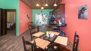 A dining area with a wooden ceiling, a kitchen in the background, and a painting on the wall. - 2-bedroom condo in West End at Sunset Villas with WiFi, AC and Ocean View (Roatan)