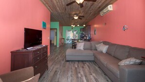 A living room with a grey sofa, wooden floor, and a ceiling fan. - 2-bedroom condo in West End at Sunset Villas with WiFi, AC and Ocean View (Roatan)