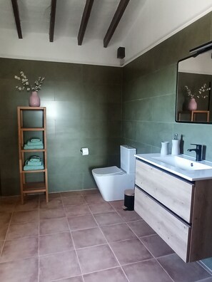 A bathroom with a wooden vanity, a toilet, and a shelf with folded towels.