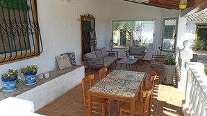Un patio exterior con una mesa de baldosas, sillas de madera, un sofá y plantas en macetas.