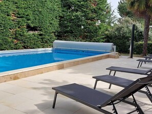 Une piscine dotée d’une terrasse carrelée et de chaises longues.