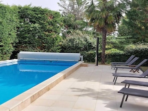 A swimming pool with a cover, surrounded by lounge chairs and dense greenery.