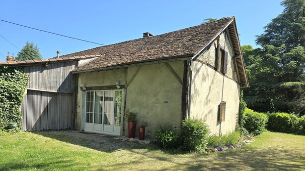Une maison rustique à deux étages, dotée d’un toit en pente, d’une porte d’entrée avec des panneaux de verre et d’un petit jardin agrémenté de plantes en pot.