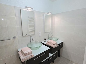A bathroom with two sinks, each with a glass bowl, a mirror above, and a towel rack.