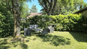 Un espace extérieur verdoyant, avec un banc et une table, entouré d’arbres et d’arbustes.