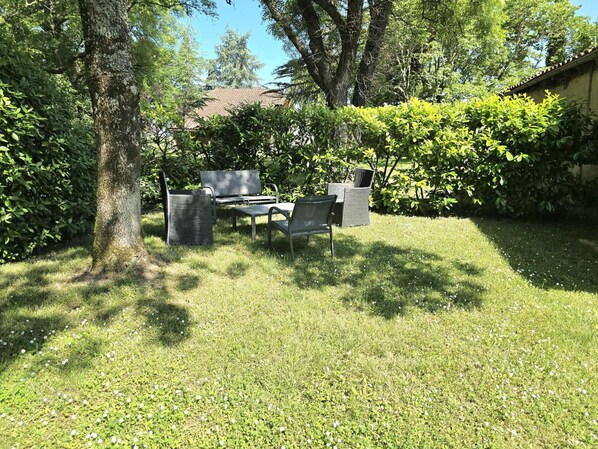 A grassy outdoor area with a bench and a table, surrounded by trees and bushes.