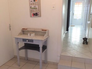 A hallway with a small white table with a box on it, a wall-mounted photo collage, and a dog on the floor. - Charming 4* Cottage in a Peaceful Vosges Hamlet (Fougerolles-Saint-Valbert)