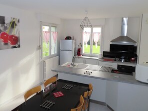 A modern kitchen with a dining table, chairs, a refrigerator, a stove, and a window with curtains.