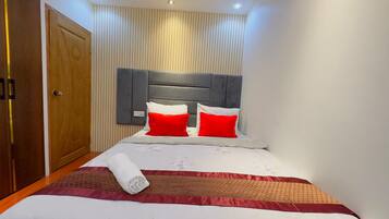 A neatly made bed with a red and white pillow set, a rolled towel, and a floral-patterned bedspread.