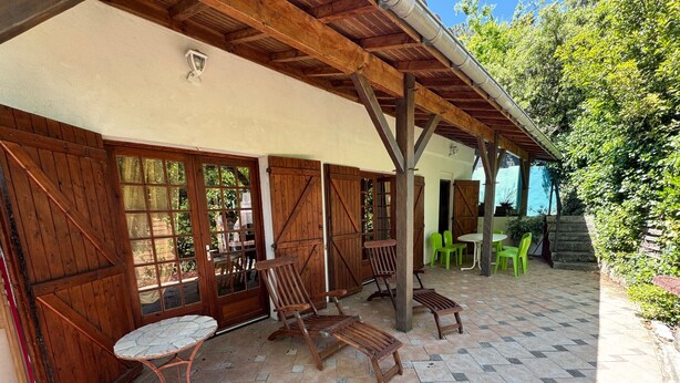A covered patio area with wooden furniture, a stone-tiled floor, and large windows.