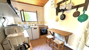 A compact kitchen with a coffee maker, a sink, a dishwasher, and a wooden table with two stools.