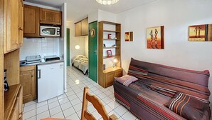 A compact living space with a kitchenette, a sofa, and artwork on the walls. - Bright studio with balcony, pets allowed (Lamalou-les-Bains)