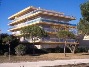 Un immeuble à plusieurs étages doté de balcons, entouré d’arbres et sous un ciel dégagé.