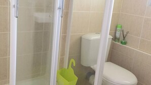 A bathroom with a shower enclosure, toilet, and a green bucket on the floor. - Beachfront apartment for 4 with parking (Argelès-sur-Mer)