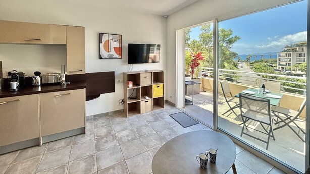 A modern kitchen with a flat-screen TV, a dining area with a round table, and a balcony with a view of the city. - 2-room apartment in Porticcio with air conditioning and parking (Porticcio)