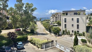A residential street with modern buildings, a clear sky, and a view of the sea. - 2-room apartment in Porticcio with air conditioning and parking (Porticcio)
